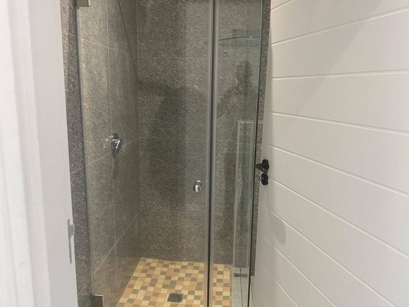 A clean, modern shower stall featuring grey stone-look wall tiles, mosaic floor tiling, and a glass enclosure, complemented by white shiplap wall paneling.