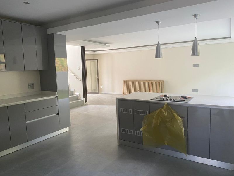 Modern open-plan kitchen and living area featuring sleek grey cabinetry, stone countertops, a built-in gas hob, and neutral tiled flooring throughout.