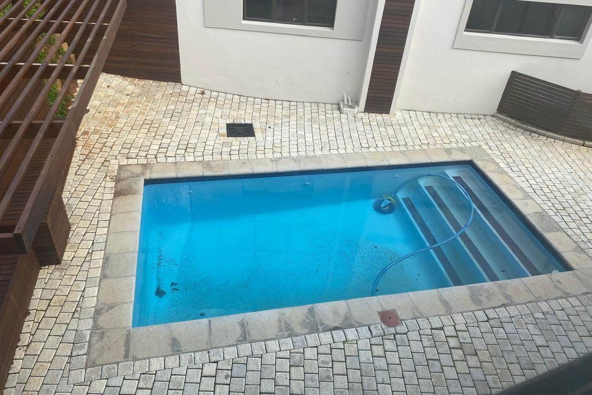 Outdoor pool area featuring a rectangular swimming pool, paved surround, and a timber pergola structure.
