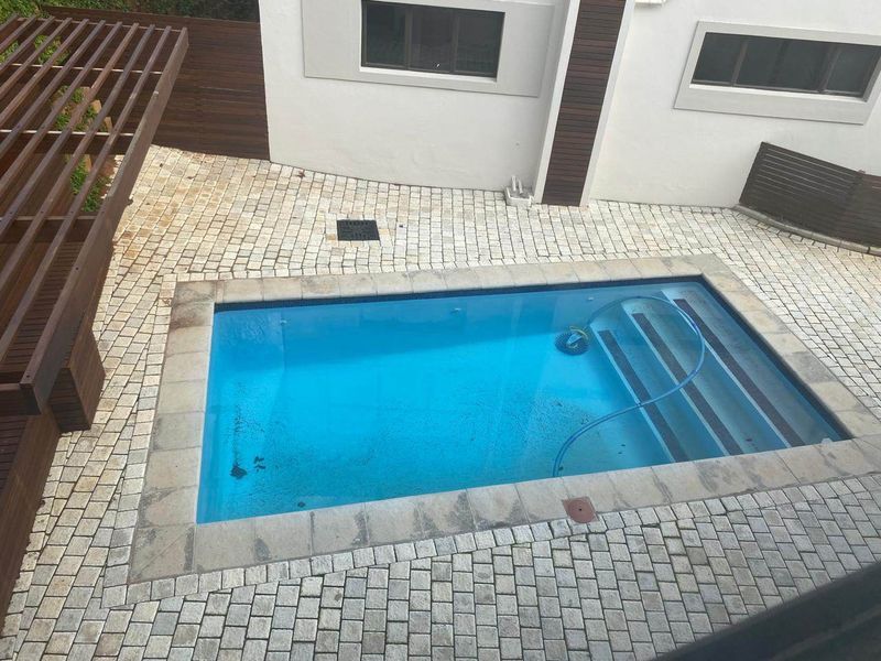 Outdoor pool area featuring a rectangular swimming pool, paved surround, and a timber pergola structure.