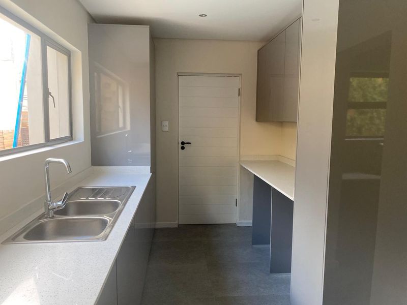 A modern, clean scullery featuring sleek grey cabinetry, stone countertops, a double bowl sink, and neutral tiled flooring.