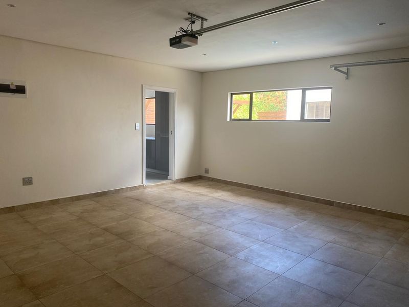 A clean, empty garage space featuring tiled flooring, a mounted garage door motor, and a horizontal window providing natural light.