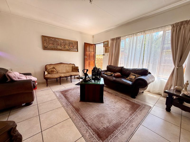 A spacious living room featuring neutral tiled flooring, large windows allowing natural light, and direct access to the exterior through a wooden door.