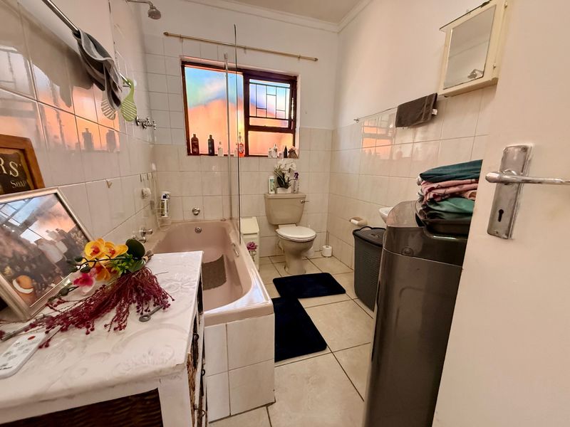 A functional bathroom featuring a bathtub with shower attachment, toilet, and tiled finishes, offering potential for modernization.