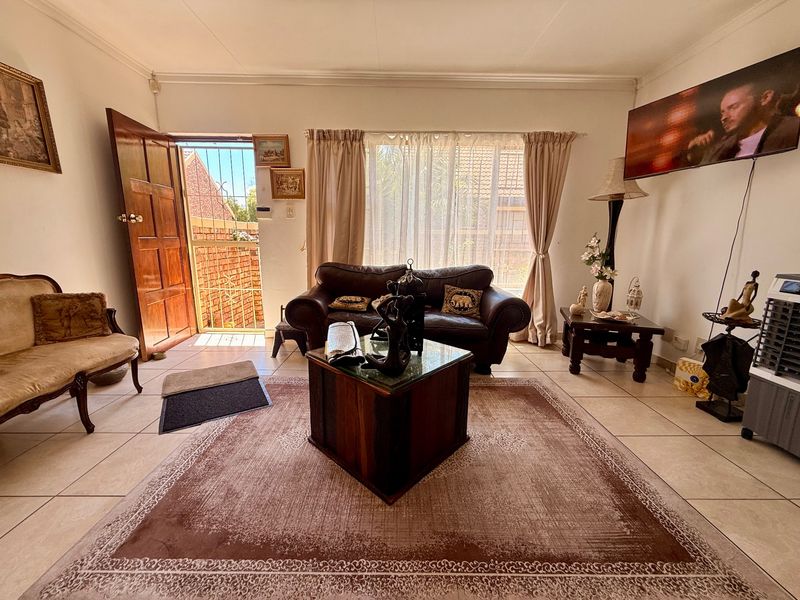 A living room featuring tiled flooring, coved ceilings, and direct access to the exterior through a timber door with a security gate.