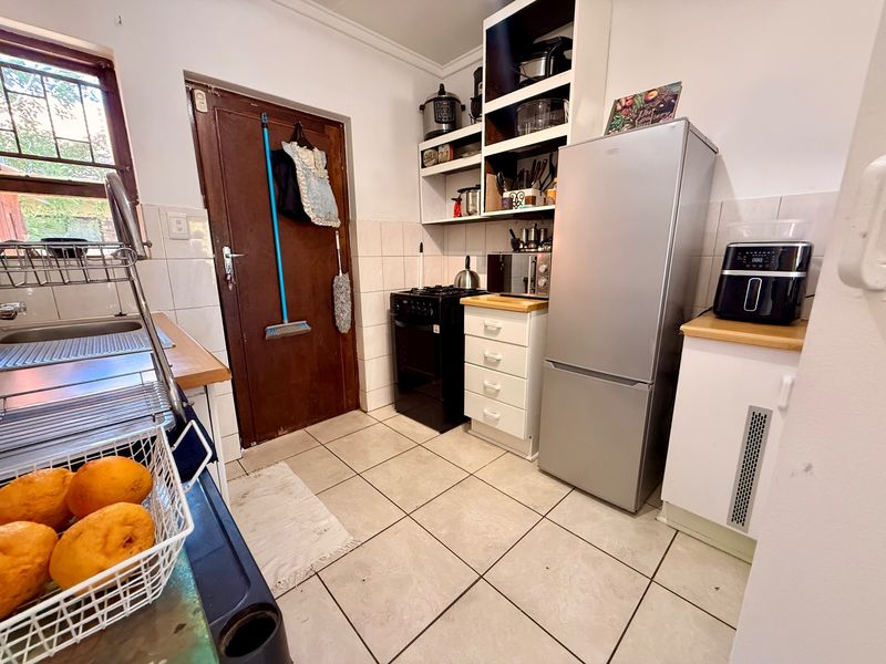 A functional kitchen featuring tiled flooring, built-in cabinetry, a gas stove, and a stainless steel sink with a rear access door.