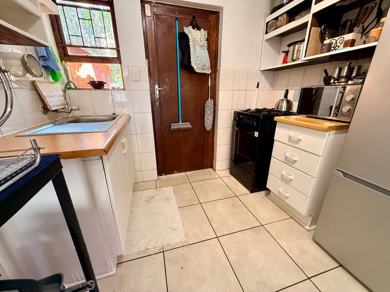 Compact kitchen featuring tiled flooring, wooden countertops, built-in cabinetry, open shelving, and a gas stove, with a rear door providing access to the exterior.