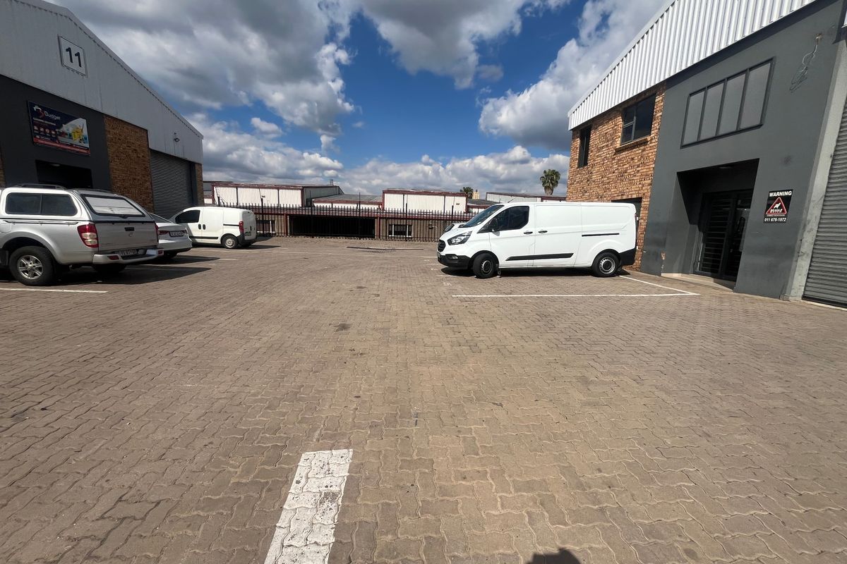 Exterior view of an industrial complex featuring paved parking area, brick and metal facade, and secure roller shutter access points.