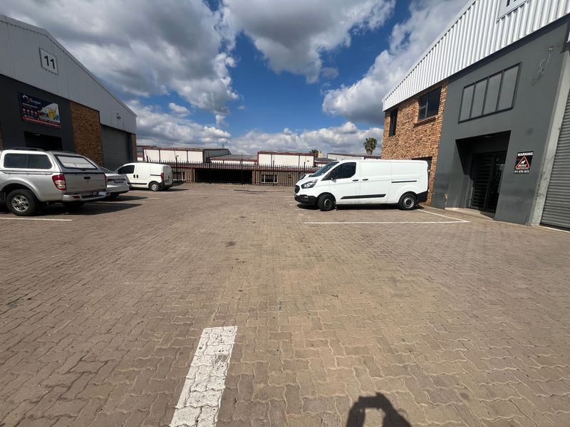 Exterior view of an industrial complex featuring paved parking area, brick and metal facade, and secure roller shutter access points.