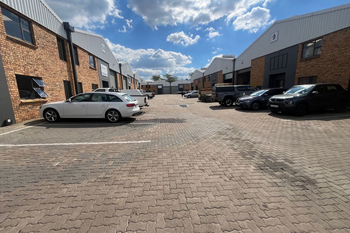 A view of an industrial complex featuring brick facades, metal roller shutter doors, and a paved parking area between the units.
