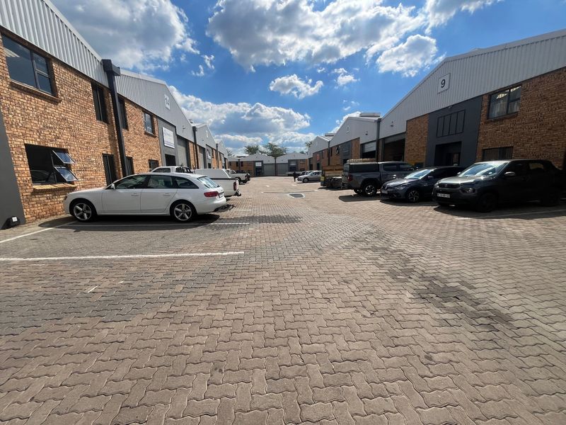 A view of an industrial complex featuring brick facades, metal roller shutter doors, and a paved parking area between the units.