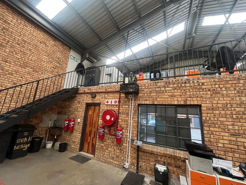 Industrial utility space featuring exposed brickwork, a steel mezzanine level with staircase, skylights, and integrated fire safety equipment.