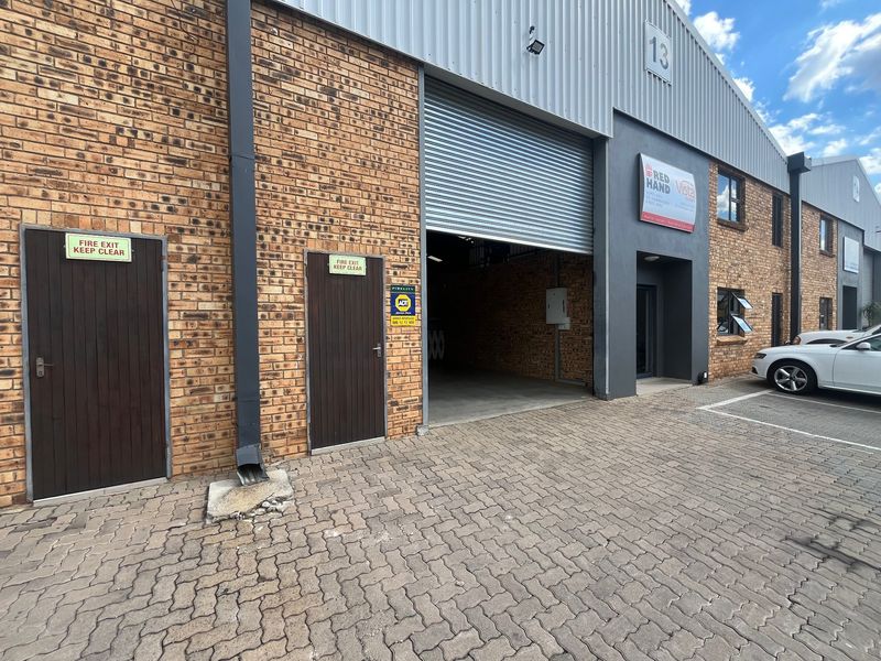 Industrial unit exterior featuring a large roller shutter door, brick facade, paved driveway, and designated fire exit access points.