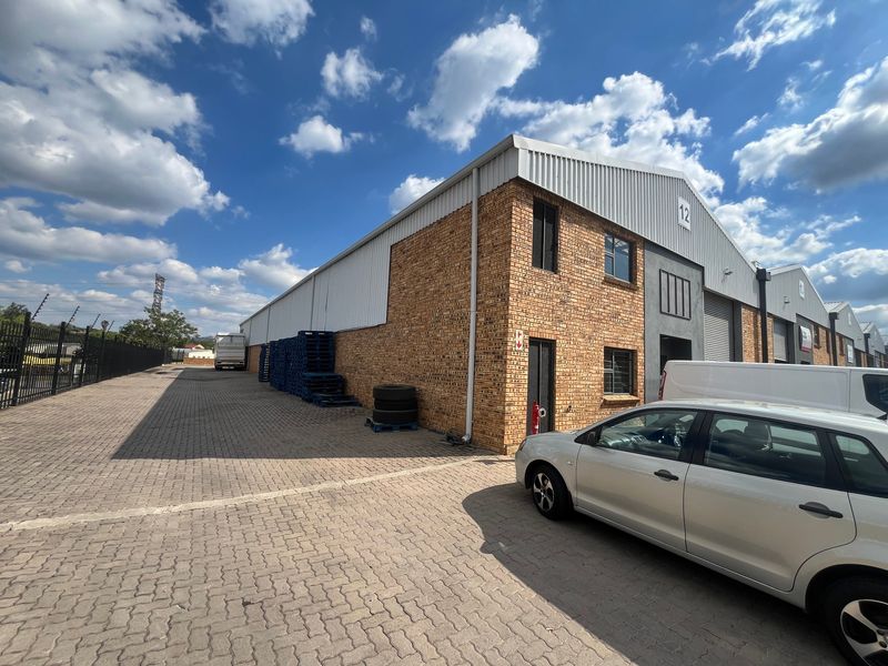 Exterior view of an industrial warehouse unit featuring face brick construction, a roller shutter door, and a paved driveway area.