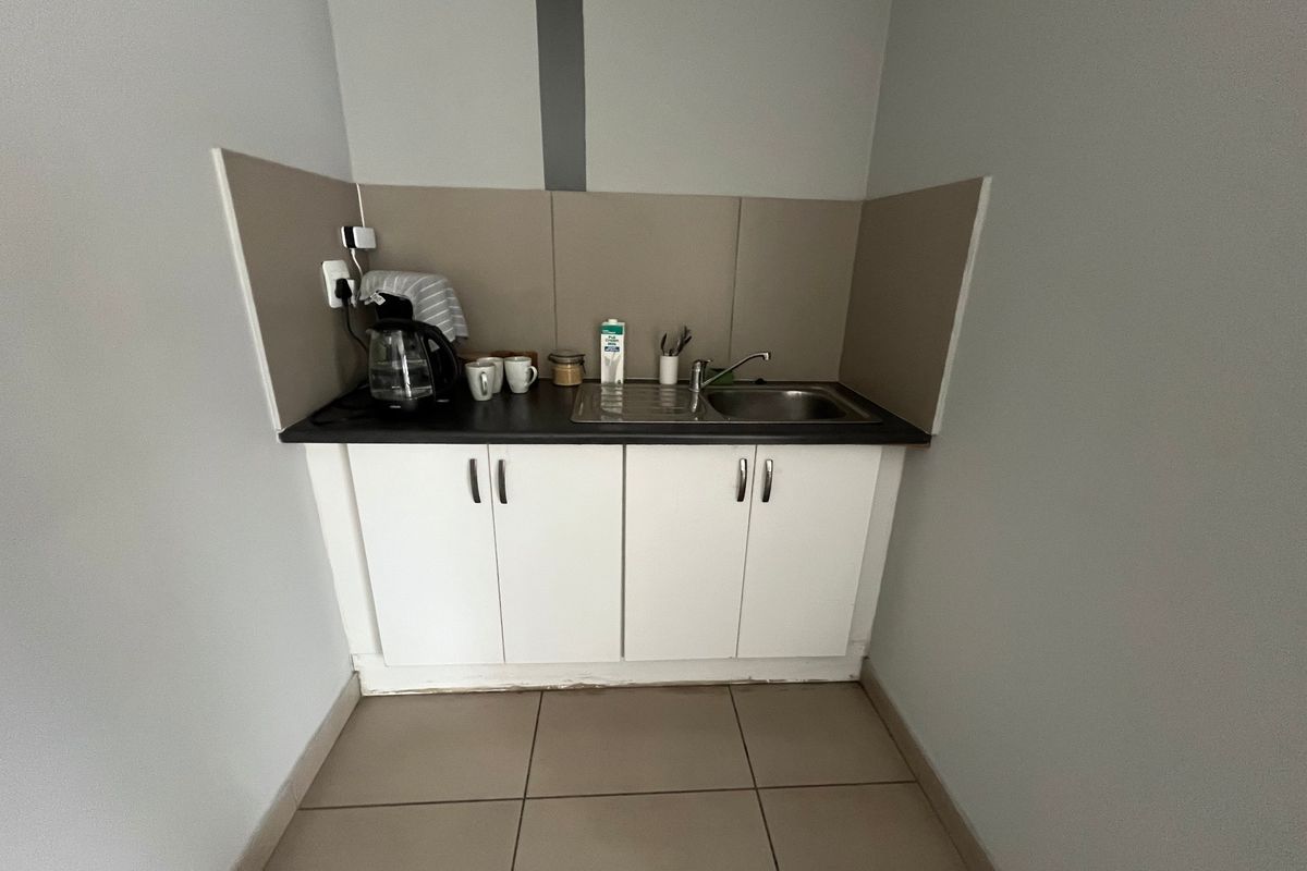 A compact kitchenette featuring white built-in cabinetry, a stainless steel sink, and tiled flooring, suitable for an office or utility space.