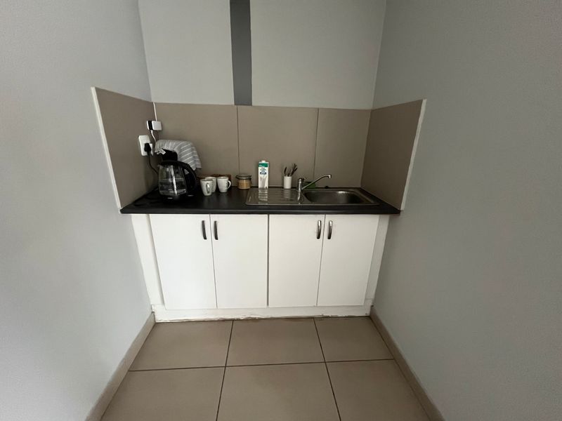 A compact kitchenette featuring white built-in cabinetry, a stainless steel sink, and tiled flooring, suitable for an office or utility space.