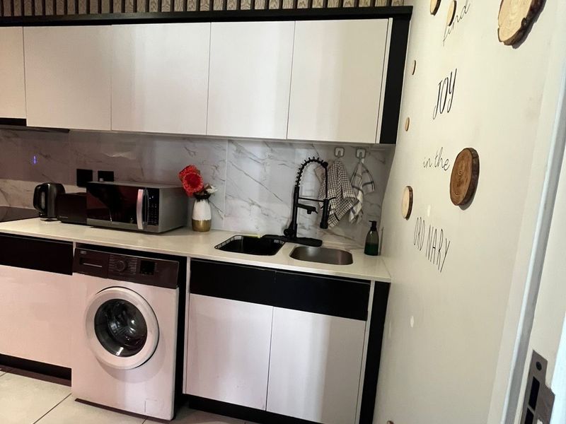 Compact kitchen featuring modern white and black cabinetry, marble-look splashback, integrated washing machine, and tiled flooring.