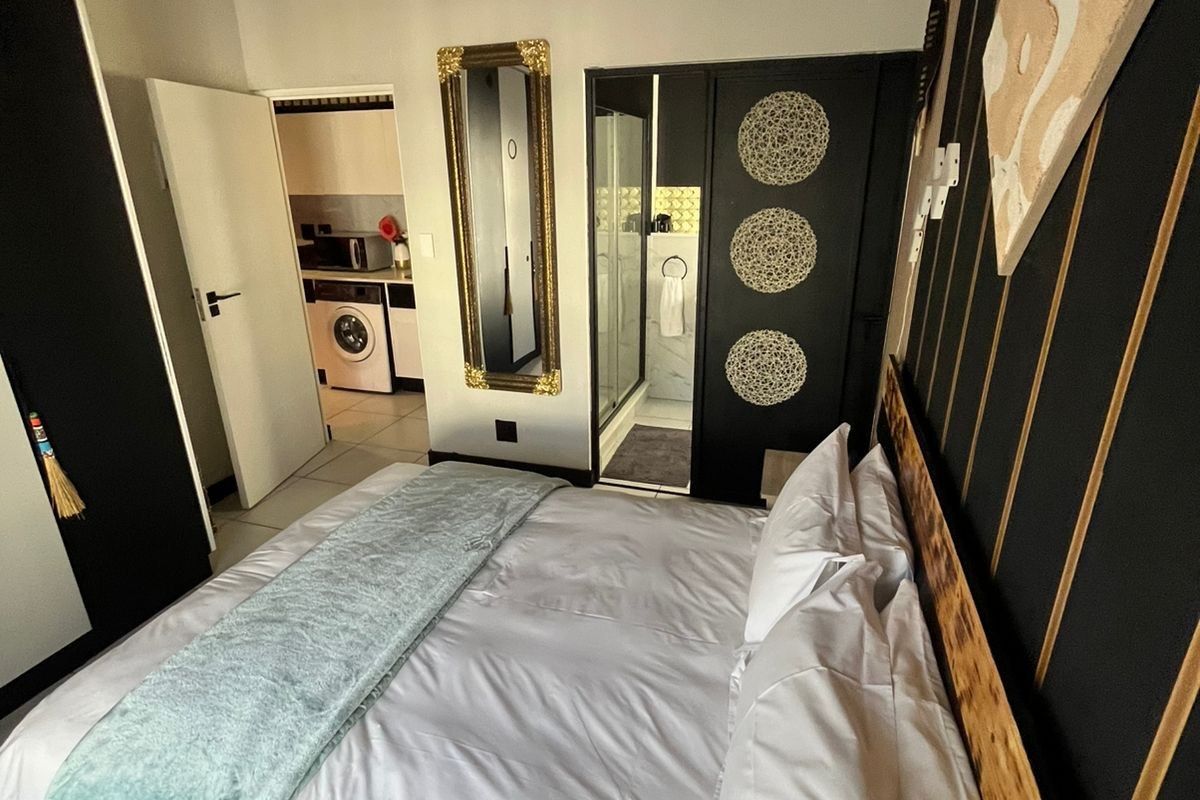 A well-maintained bedroom featuring a unique slatted timber ceiling, tiled flooring, and direct access to an en-suite bathroom and laundry area.