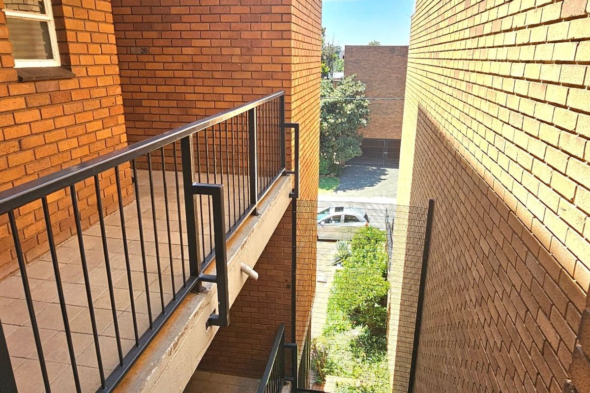 View of the apartment building exterior showing brick facade, metal balustrades, and tiled walkways between building blocks.