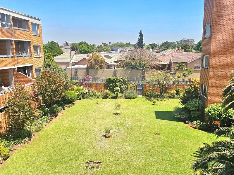 Elevated view of a well-maintained communal garden area situated between two brick apartment buildings, featuring established landscaping and a perimeter boundary wall.