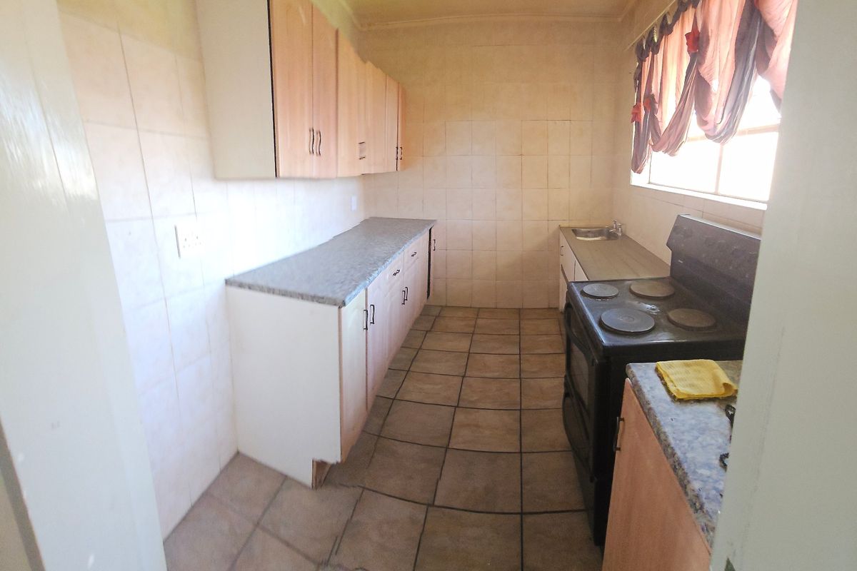 A functional kitchen featuring laminate countertops, built-in cabinetry, tiled splashbacks, and a freestanding stove, offering potential for modernization and aesthetic updates.
