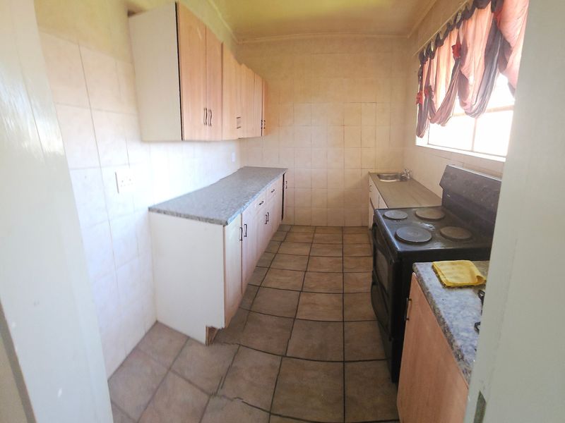 A functional kitchen featuring laminate countertops, built-in cabinetry, tiled splashbacks, and a freestanding stove, offering potential for modernization and aesthetic updates.