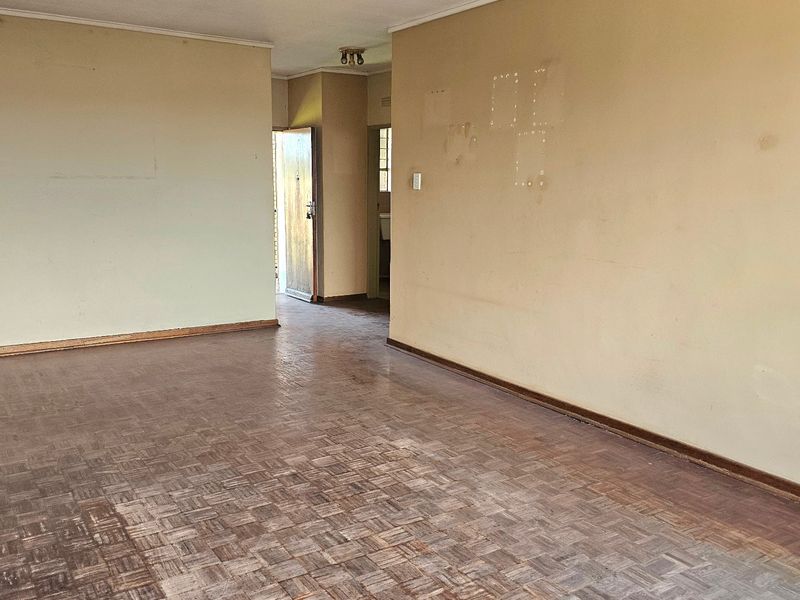 An empty living room featuring original parquet flooring and neutral walls, requiring cosmetic updates to restore its appeal.