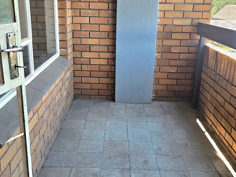 A compact balcony featuring exposed brick walls, tiled flooring, and a metal railing, offering a functional outdoor space.