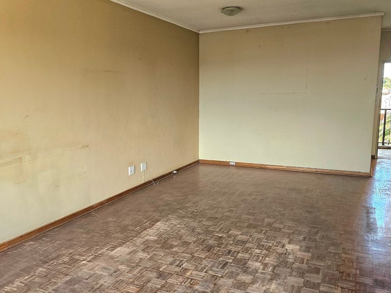 An empty living room featuring original parquet flooring, neutral wall finishes, and direct access to an outdoor balcony area.