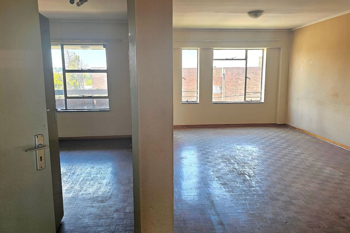 Spacious, empty living area featuring original parquet flooring and large steel-framed windows, offering a blank canvas for renovation and modernization.