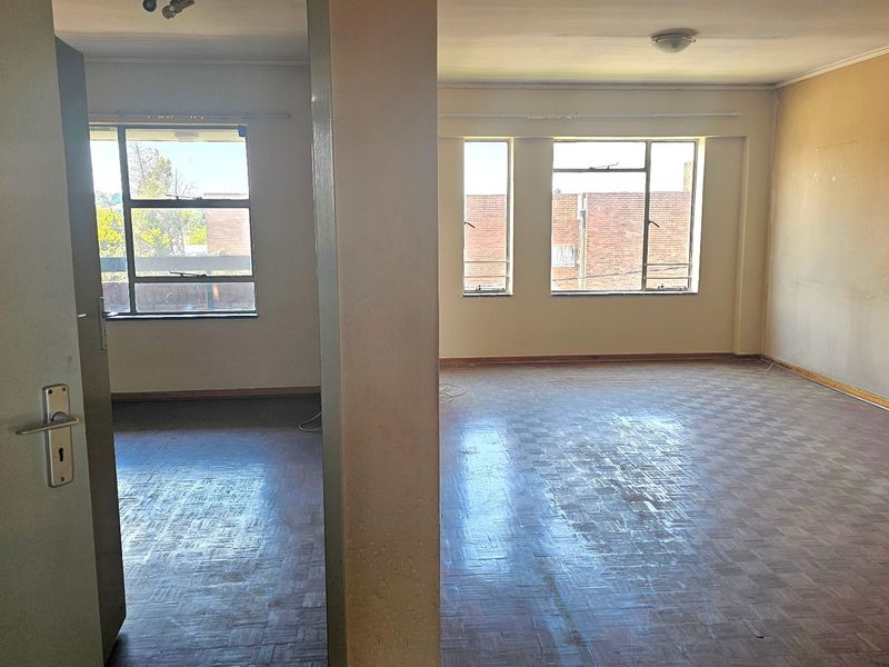 Spacious, empty living area featuring original parquet flooring and large steel-framed windows, offering a blank canvas for renovation and modernization.