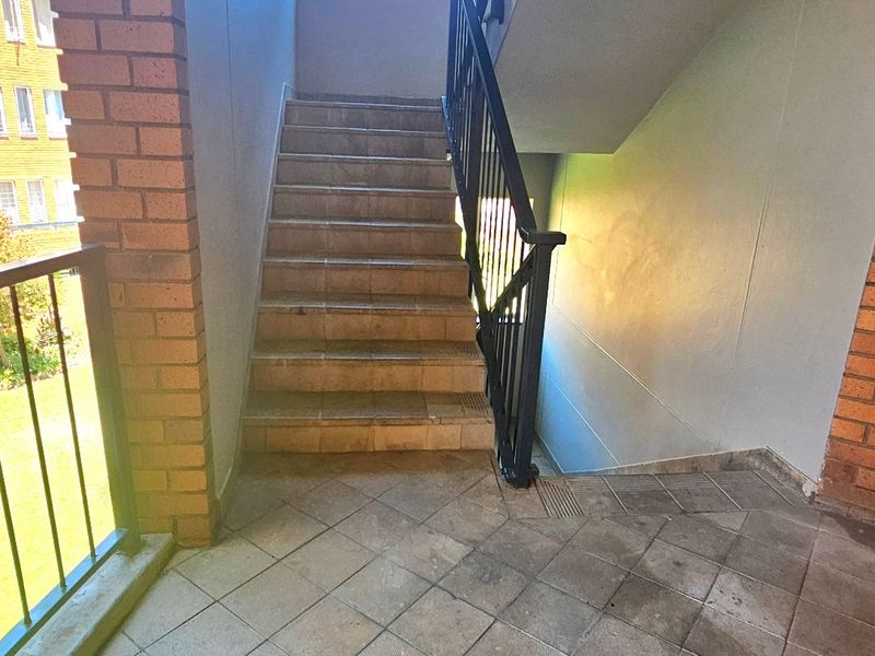 A functional apartment stairwell featuring tiled steps, a metal balustrade, and brick accents, providing access between building levels.