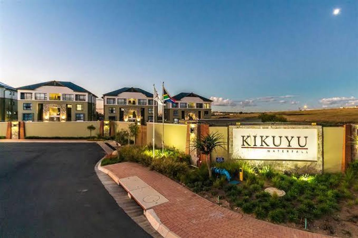 The entrance facade of the Kikuyu Waterfall apartment complex, featuring a prominent signage wall, paved walkways, and well-maintained landscaped grounds.