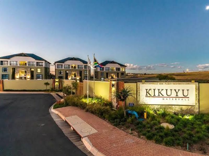 The entrance facade of the Kikuyu Waterfall apartment complex, featuring a prominent signage wall, paved walkways, and well-maintained landscaped grounds.