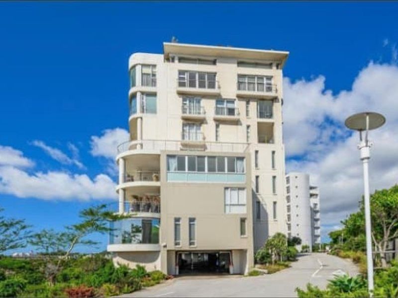 A modern multi-story apartment building featuring private balconies, integrated undercover parking, and well-maintained exterior finishes set in a landscaped environment.
