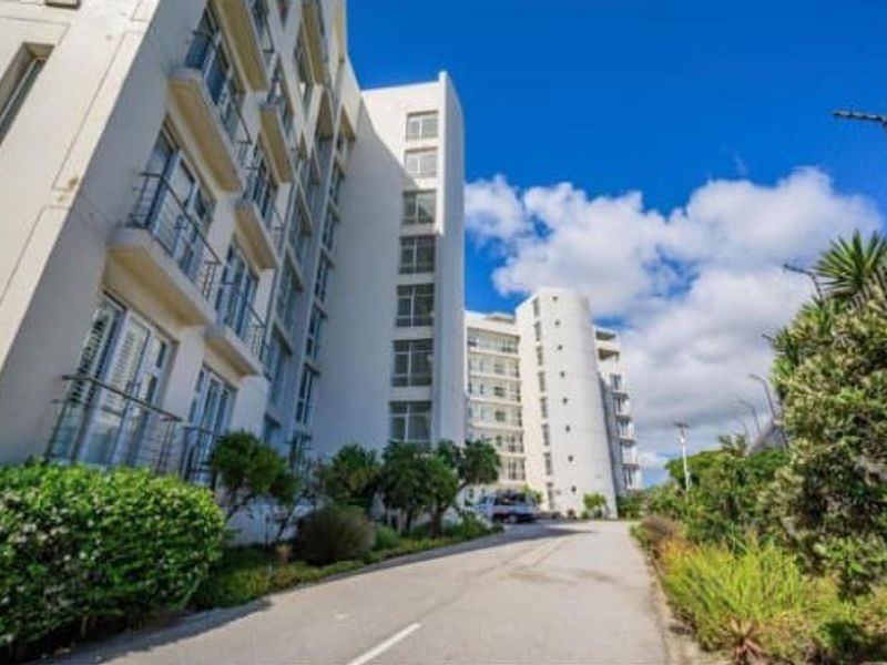 Exterior view of a multi-story apartment building featuring balconies, a paved driveway, and perimeter electric fencing.