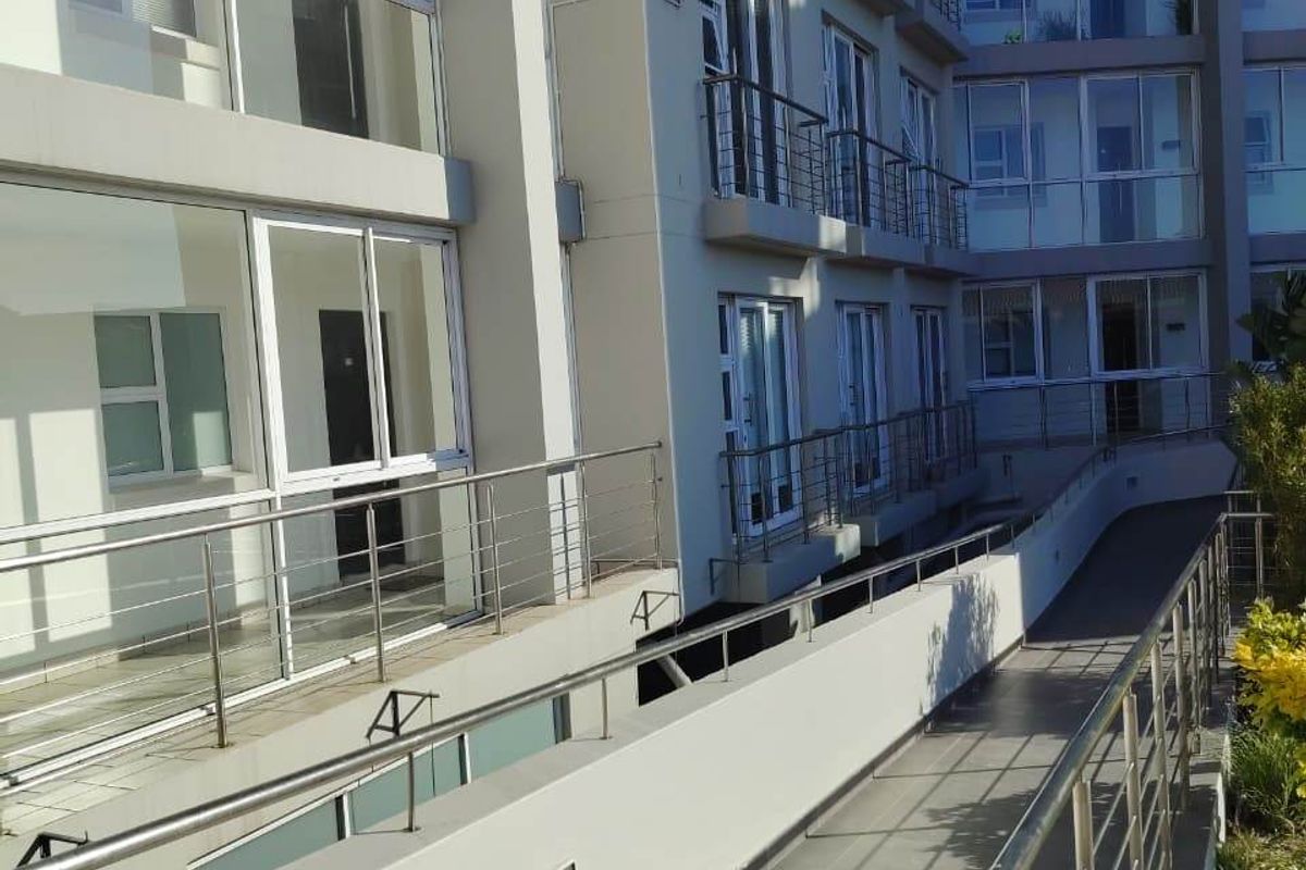 Exterior view of an apartment building featuring a modern tiled ramp with stainless steel balustrades and multiple levels of glass sliding doors.