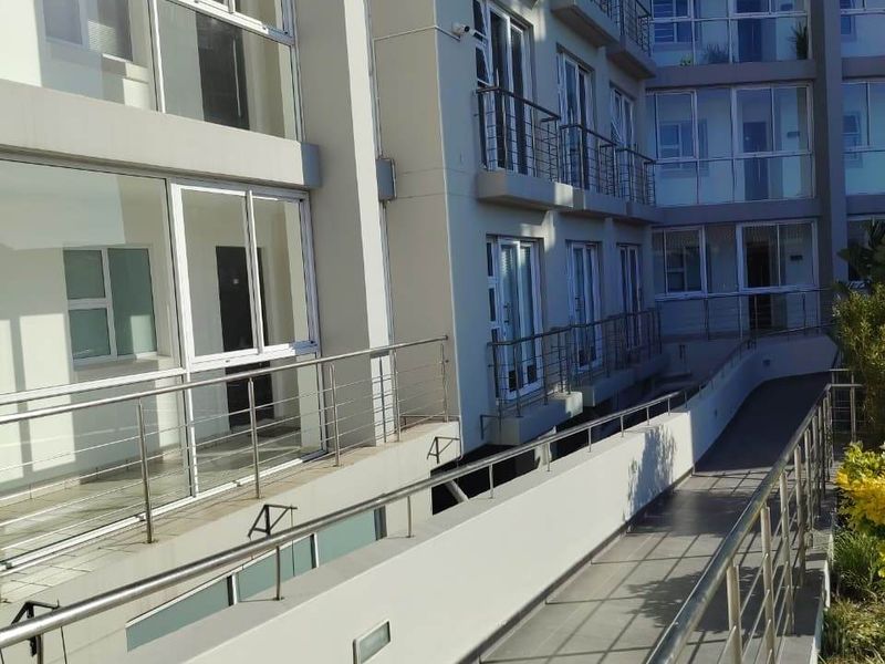 Exterior view of an apartment building featuring a modern tiled ramp with stainless steel balustrades and multiple levels of glass sliding doors.