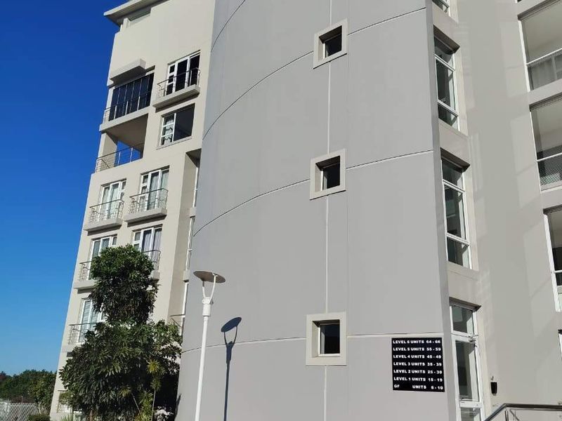 Exterior view of a modern apartment building facade featuring a curved architectural design, balconies, and clear unit level signage.