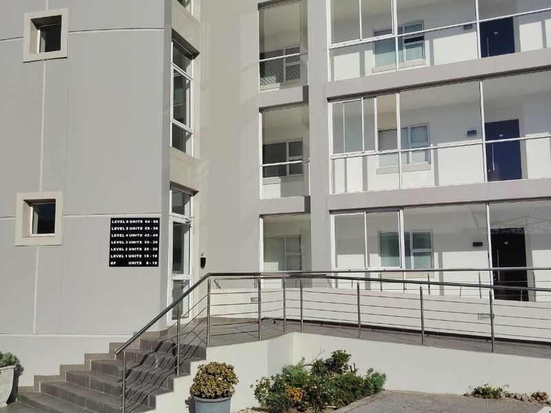 Exterior view of a modern apartment building featuring a paved entrance, staircase with metal handrails, and multiple levels of balconies with sliding glass doors.