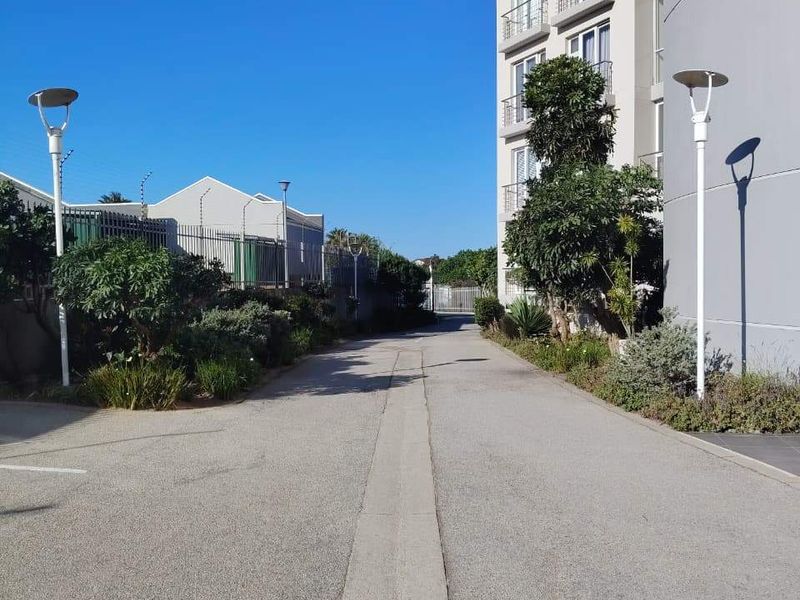 A clear view of the apartment complex exterior, featuring a paved driveway, landscaped garden borders, and modern perimeter lighting.
