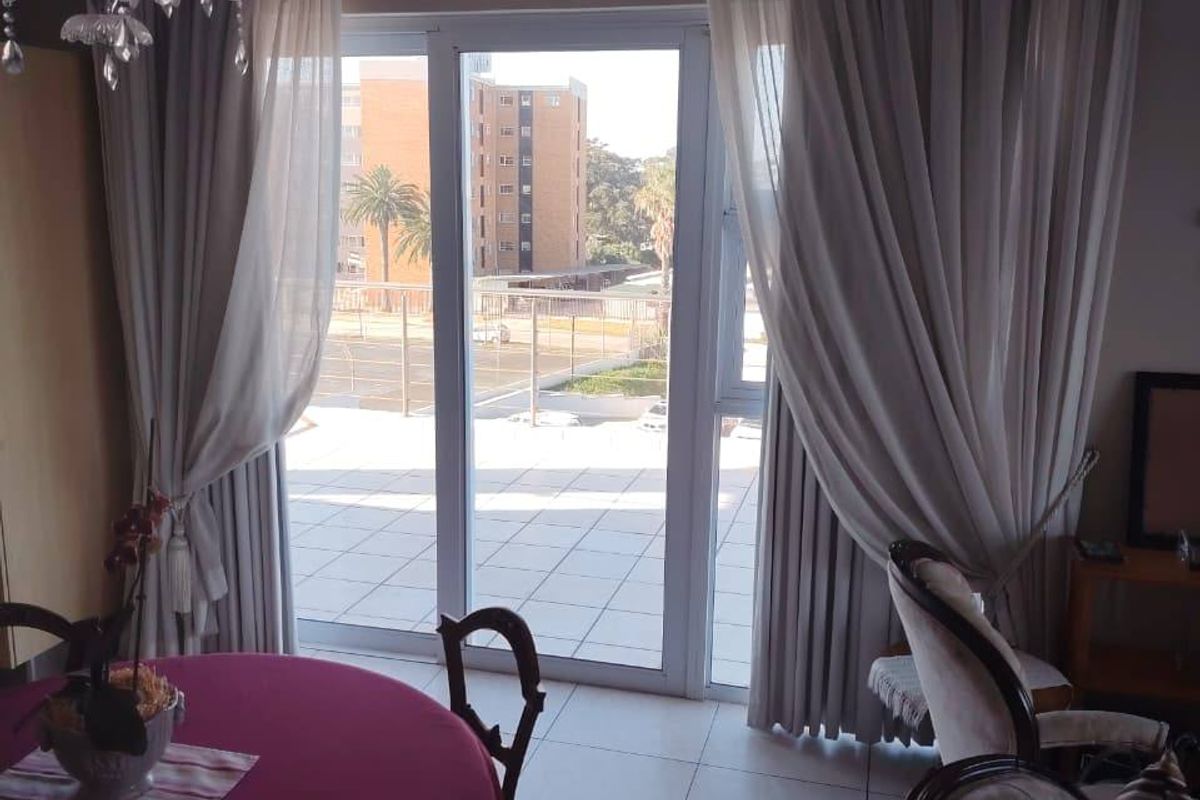 A bright living area featuring tiled flooring and a large sliding glass door providing access to an outdoor balcony.