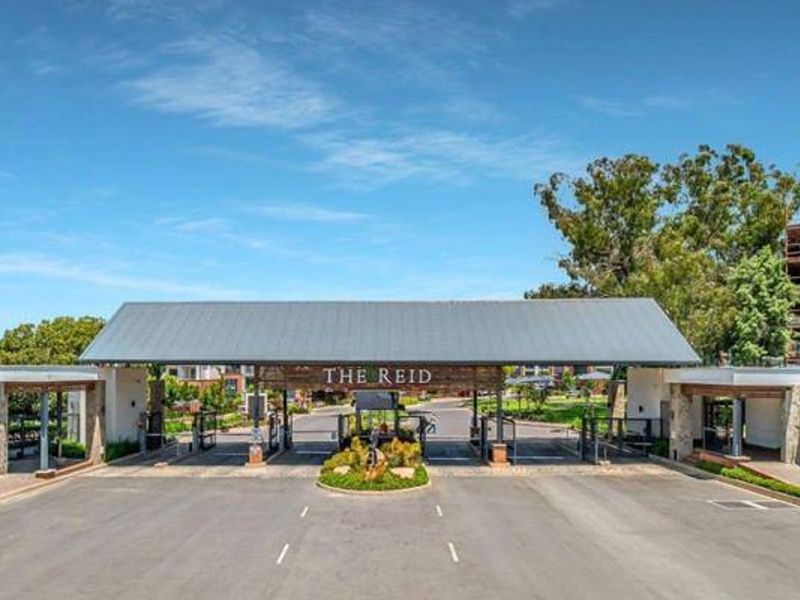 The secure entrance gatehouse of The Reid apartment complex, featuring modern stone cladding, metal roofing, and controlled access points.