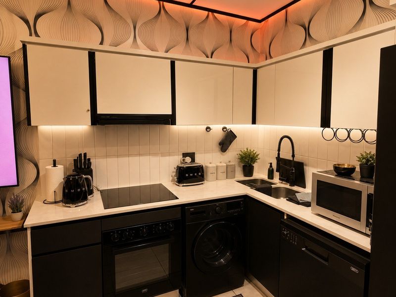 Modern compact kitchen featuring sleek black and white cabinetry, integrated appliances, tiled backsplash, and ambient under-cabinet lighting.