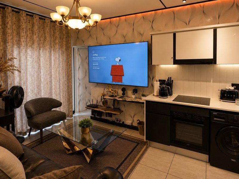 Modern open-plan living area featuring a compact kitchen with built-in appliances, tiled flooring, and contemporary lighting, seamlessly integrated with the lounge space.