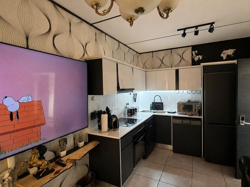 A modern, compact kitchen featuring high-contrast black and white cabinetry, integrated appliances, tiled flooring, and a decorative patterned wallpaper finish.