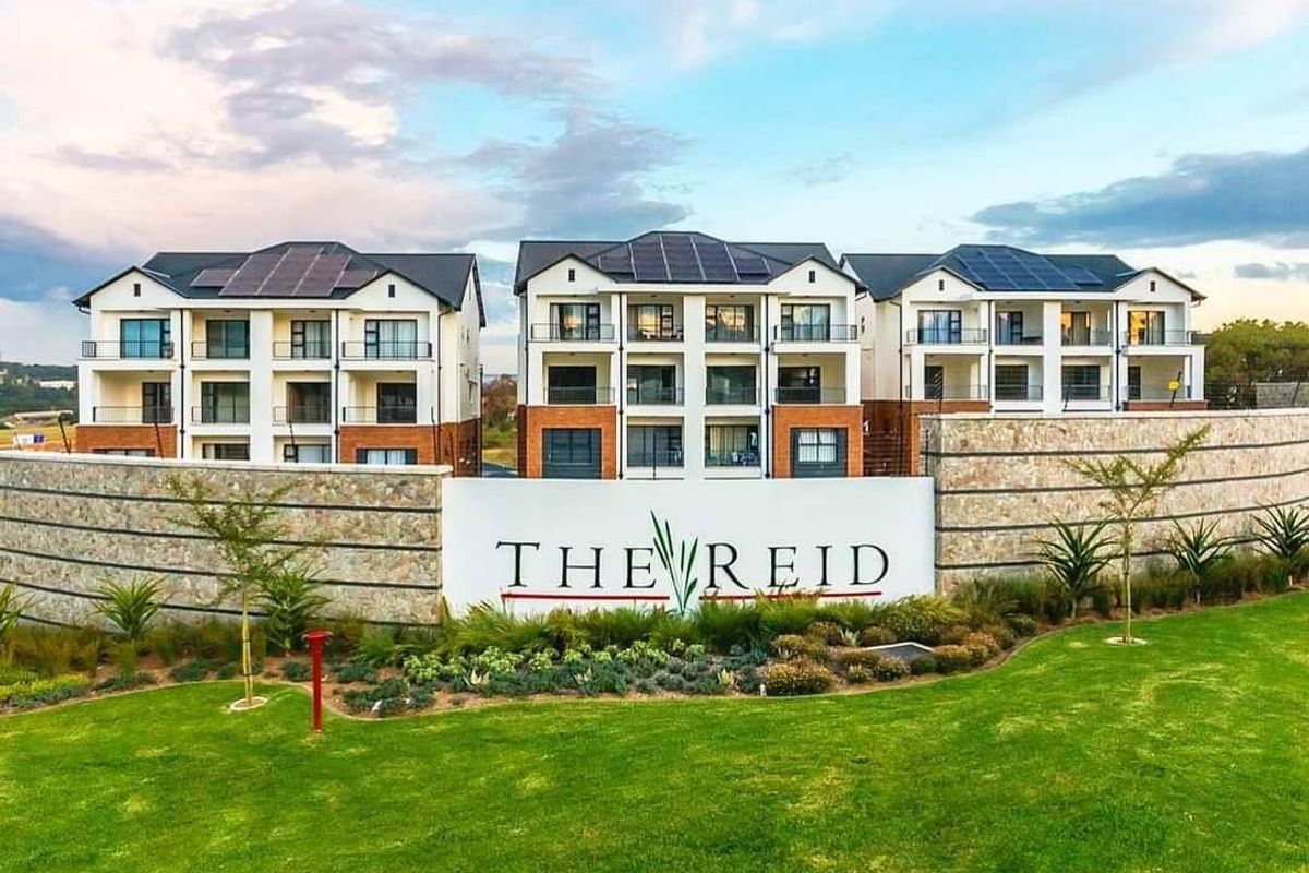 Aerial view of The Reid apartment complex featuring modern multi-story buildings with solar panels, stone-clad retaining walls, and well-maintained landscaped gardens.
