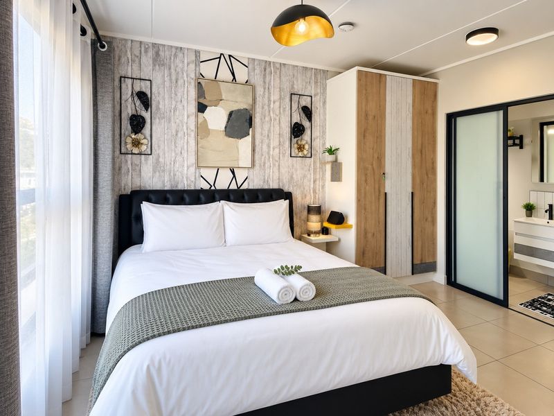 A modern bedroom featuring a built-in wardrobe, tiled flooring, and an en-suite bathroom accessible via a sliding door.