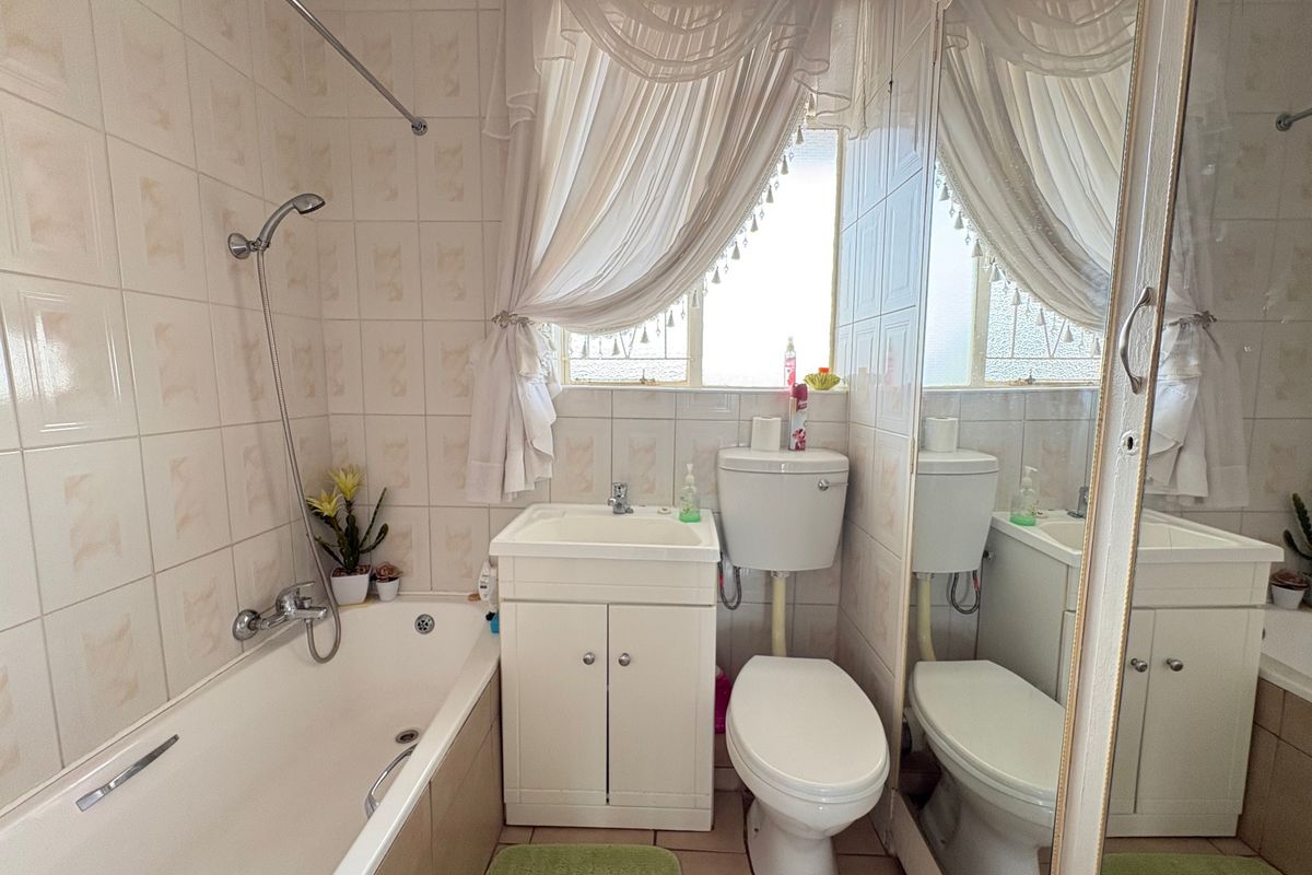 A compact bathroom featuring a bathtub with shower mixer, vanity basin, and toilet, finished with neutral wall and floor tiling.