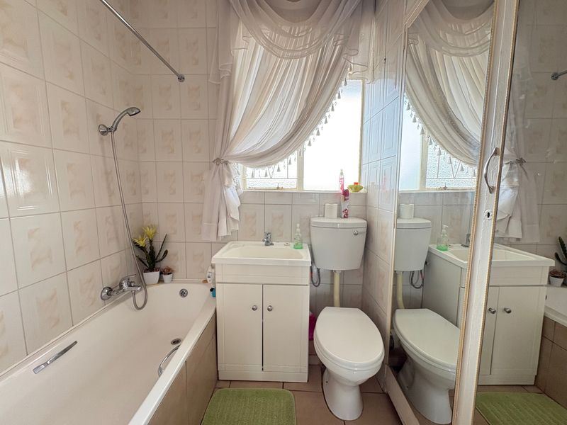 A compact bathroom featuring a bathtub with shower mixer, vanity basin, and toilet, finished with neutral wall and floor tiling.